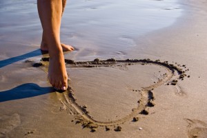 Girl drawing an heart in the sand.